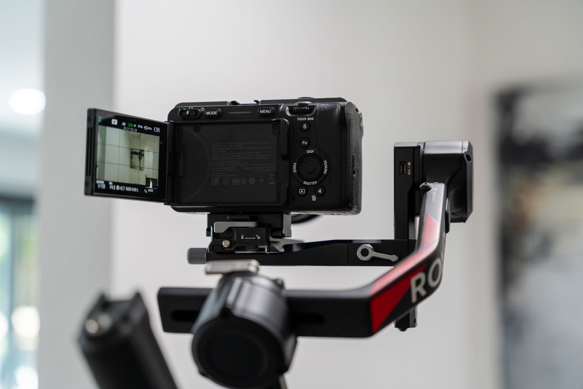 Digital camera mounted on gimbal with open screen in a well-lit room.